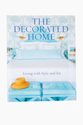 Book cover of The Decorated Home by Meg Braff, published by Rizzoli, showcasing a blue and white bedroom in her signature style with a hat on a bench at the bed's foot.