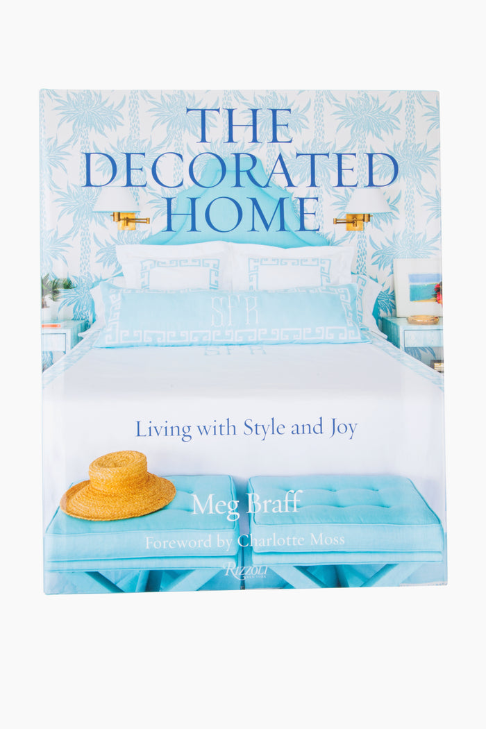 Book cover of The Decorated Home by Meg Braff, published by Rizzoli, showcasing a blue and white bedroom in her signature style with a hat on a bench at the bed's foot.