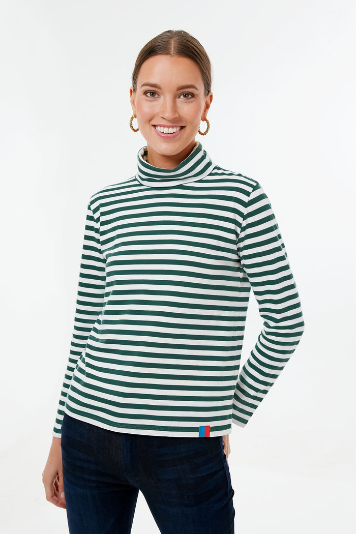 A woman in a black and white stripe KULE turtleneck long-sleeve shirt and dark pants smiles at the camera, showcasing this perfect layering piece.