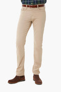 A person wearing beige premium denim pants by AG Jeans, paired with a brown belt, brown boots, and a plaid shirt, shown from the shoulders down.