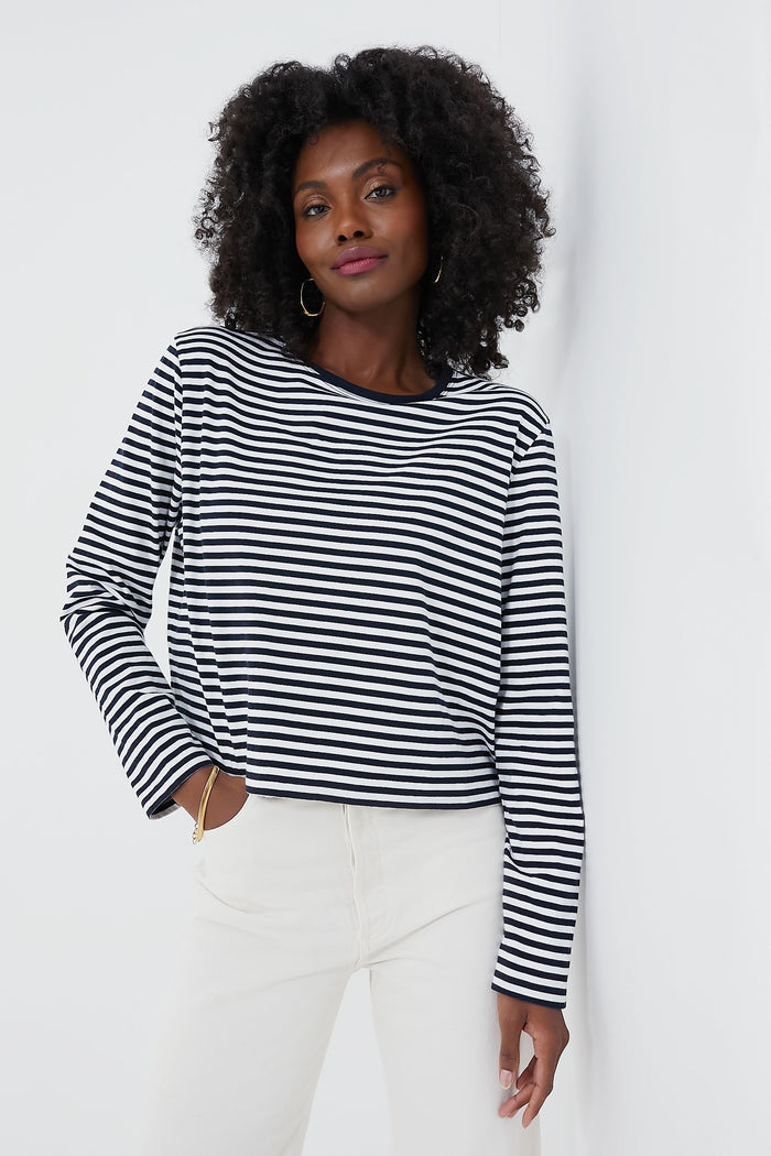 A woman wears the KULE Venice Tee—a classic black and white long-sleeve striped top—paired with white pants.