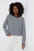 A woman wears the KULE Venice Tee—a classic black and white long-sleeve striped top—paired with white pants.