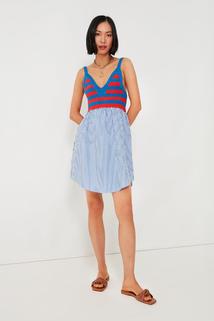 A woman wears a KULE stripe dress with a blue, red, and gray crochet bodice and a blue-and-white striped skirt, paired with brown sandals.