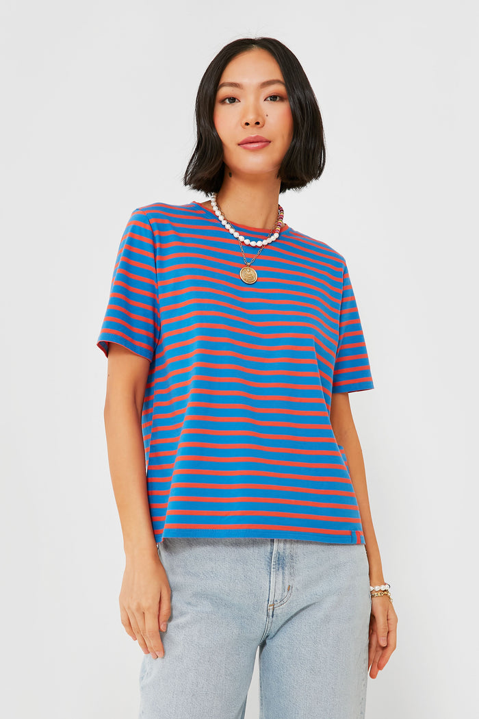 A woman stands confidently in a KULE blue and red stripe tee, light blue jeans, layered necklaces, and bracelets.
