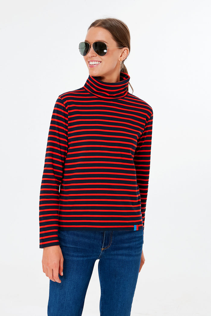 Woman wearing aviator sunglasses, a KULE cotton turtleneck for women with red and navy stripes, and blue jeans, standing confidently.