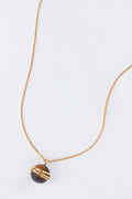 This Tuckernuck Jewelry gold chain necklace showcases a round dark stone pendant wrapped in gold wire, blending vintage inspiration with elegance and timeless charm.