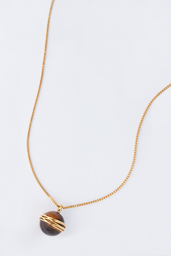 This Tuckernuck Jewelry gold chain necklace showcases a round dark stone pendant wrapped in gold wire, blending vintage inspiration with elegance and timeless charm.