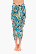 Barefoot individual wears a Ulla Johnson patterned cotton viscose sarong coverup in teal, green, and beige, tied at the waist. Photo captures from shoulders to feet.