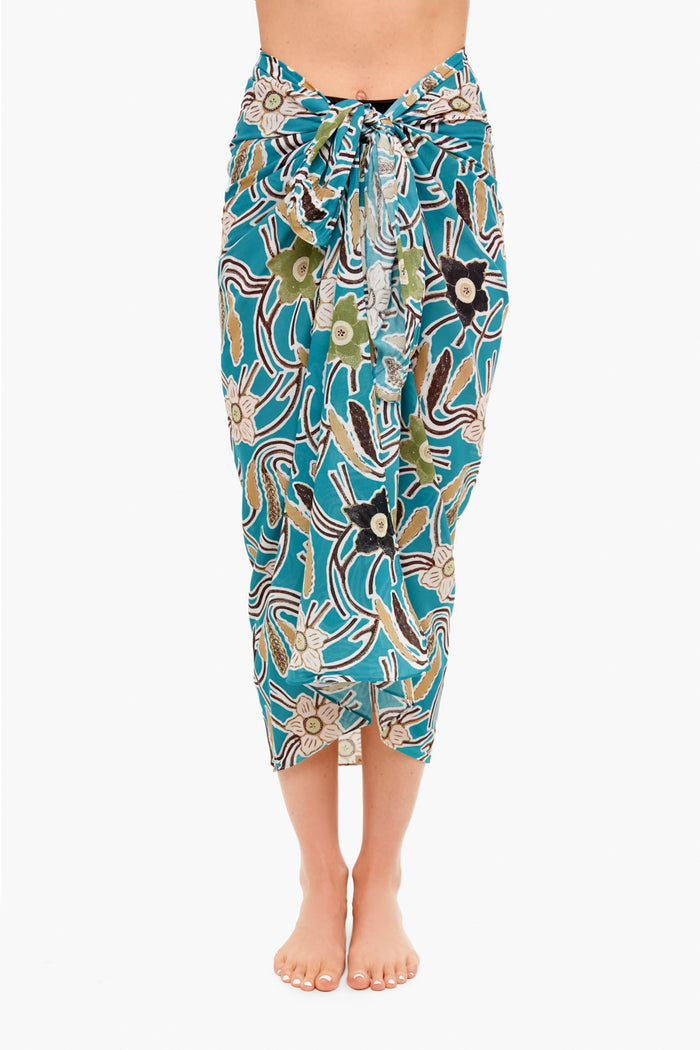 Barefoot individual wears a Ulla Johnson patterned cotton viscose sarong coverup in teal, green, and beige, tied at the waist. Photo captures from shoulders to feet.