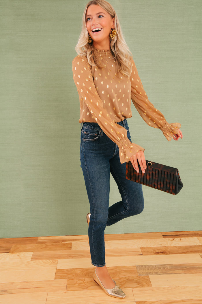 Model mid-stride, wearing classic metallic gold ballet flats and holding the high-end Tortoise Iris Clutch, effortlessly pairing with fun, sheer blouse and dark jeans.