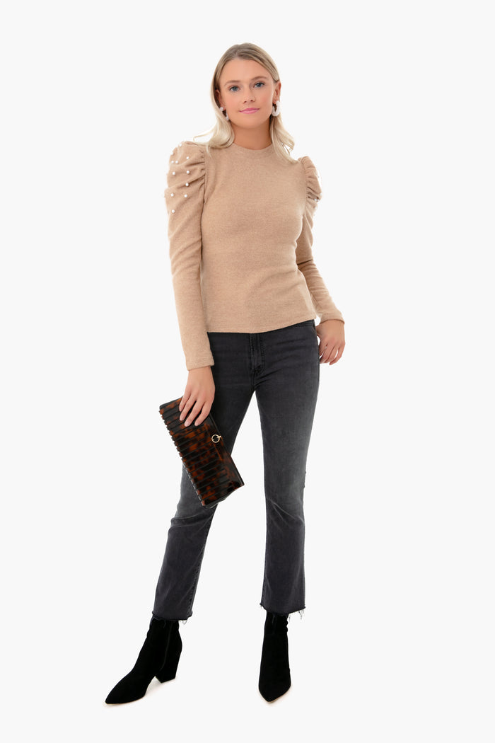 A young woman holds the classic, high-end Tortoise Iris Clutch, effortlessly paired with a light camel sweater and dark jeans, embodying a fun, confident style.