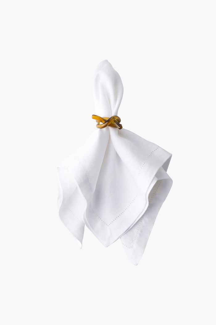 A white cloth napkin is held by a Juliska amber napkin ring, adding a touch of elegance and charm.