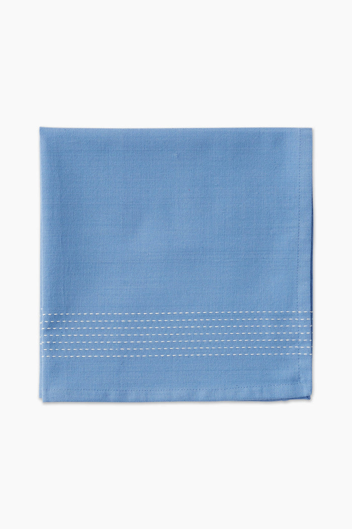A folded light blue cotton napkin by Caton's Wharf, featuring three rows of white edge stitching, adds a touch of coastal table decor.