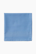 A folded light blue cotton napkin by Caton's Wharf, featuring three rows of white edge stitching, adds a touch of coastal table decor.