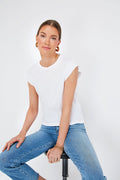 A woman in a classic white t-shirt and blue jeans sits on a stool, embodying the effortless style of THE GREAT. Peak Shoulder Tee, handcrafted in LA.