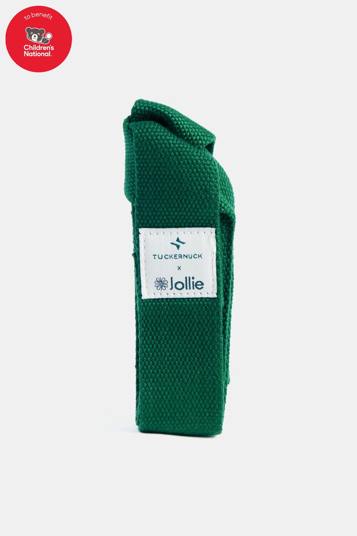 A green fabric Tuckernuck x Jollie yoga mat case with a white label stands upright; a red Children’s National benefit logo is in the top left corner.