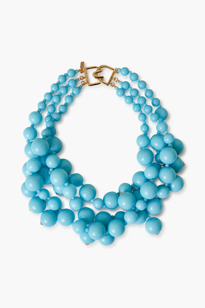 A chunky turquoise cluster necklace by Kenneth Jay Lane features three strands of large and small round beads with a gold clasp—an eye-catching piece of costume jewelry.