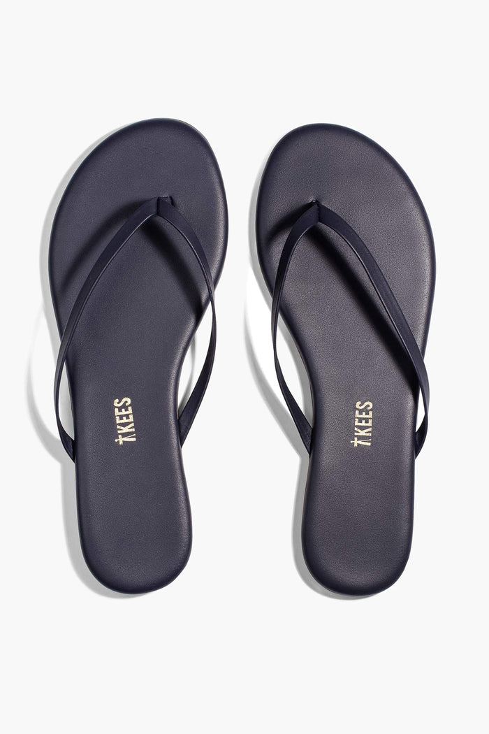 A pair of TKEES flip-flops in dark navy blue leather with thin straps, made in Brazil.