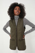 A woman stands with her hands on her hips, wearing a black-and-white striped turtleneck and a Barbour olive Polarquilt Waistcoat.