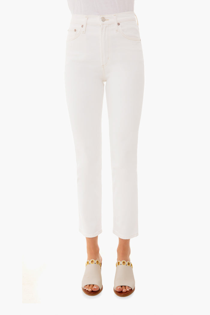 A person stands confidently in white AGOLDE mid-rise straight jeans and white sandals with gold accents.