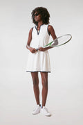 A woman in a Tnuck Sport white and navy tennis dress with sneakers holds a racket, showcasing sporty style.