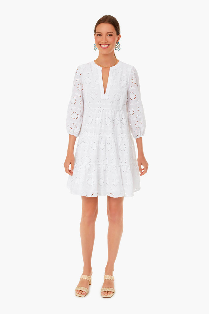 A woman stands facing forward, smiling in a white, knee-length eyelet tunic dress with three-quarter sleeves by Sail to Sable and beige wedge sandals—an effortlessly chic choice for women’s resort wear. Her hair is pulled back.