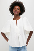 A woman wears a Pomander Place white cotton blouse with short flutter sleeves and a V-neckline, paired with light blue jeans.