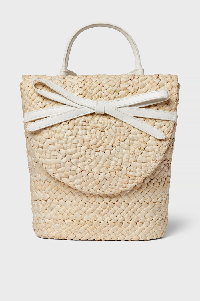 The BTB woven straw handbag boasts a boho-chic style with a round flap, white handles, and a decorative white bow detail on the front.