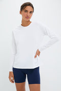A woman wears a Tnuck Sport white Long Sleeve Ryan Boyfriend Tee with SPF protection and navy blue shorts, posing with one hand on her hip.