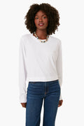 A woman wears a relaxed fit, long-sleeve white Z SUPPLY shirt, blue jeans, and a beaded necklace—perfect for everyday essentials.