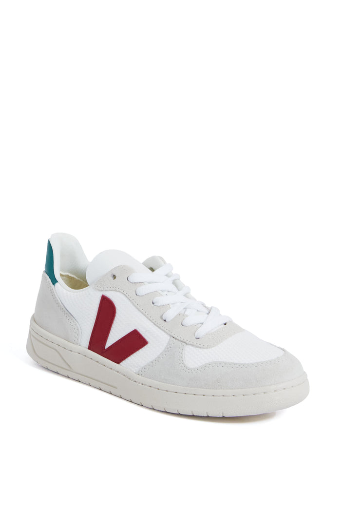 The VEJA low-top sneaker features a white design with light gray suede accents, a red V logo on the side, and a teal heel patch, all crafted from eco-friendly materials.