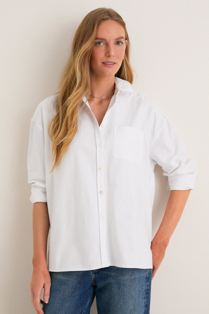 Person models the classic White Oxford Adair Boyfriend Shirt, effortlessly styled with rolled sleeves and high-low hem, paired with medium-wash jeans for a high-end, fun look.