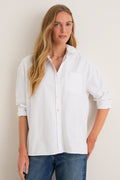 Person models the classic White Oxford Adair Boyfriend Shirt, effortlessly styled with rolled sleeves and high-low hem, paired with medium-wash jeans for a high-end, fun look.