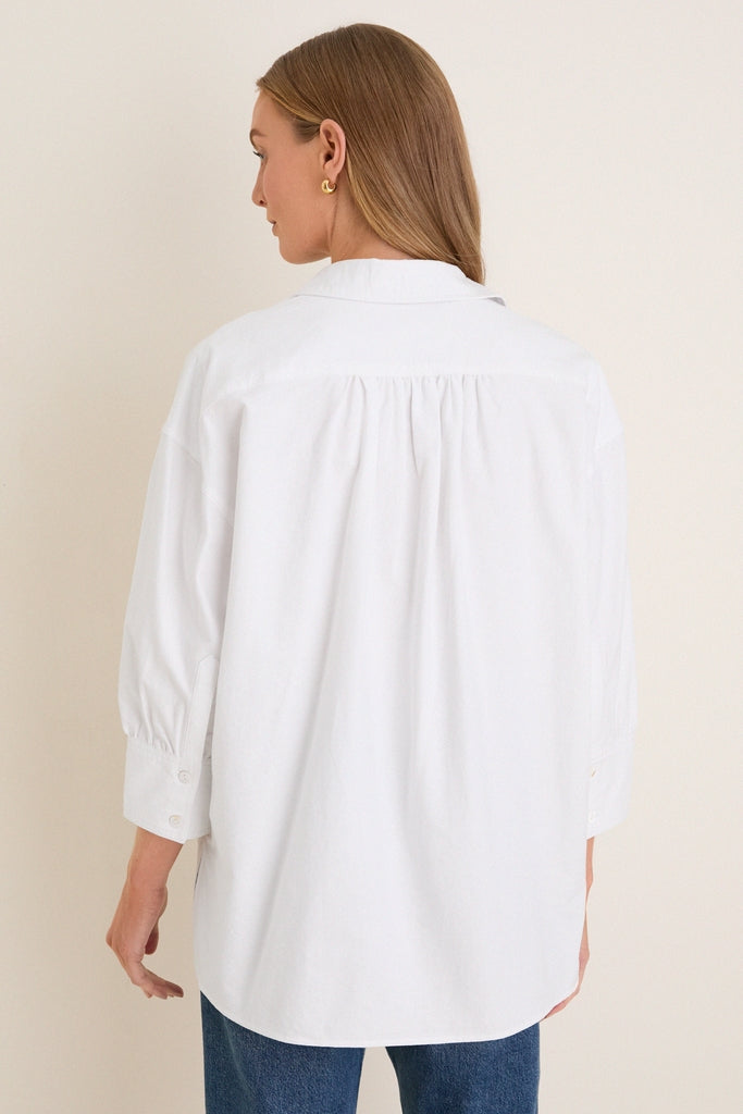 Model wearing the classic White Oxford Adair Boyfriend Shirt with buttoned cuffs and a high-low hem, epitomizing effortless, high-end style, paired with medium-wash jeans.