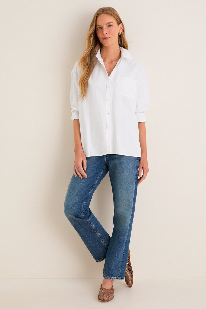 Woman models the White Oxford Adair Boyfriend Shirt, a classic, effortless piece with a high-low hem and bracelet sleeves, perfect for a fun, high-end look.