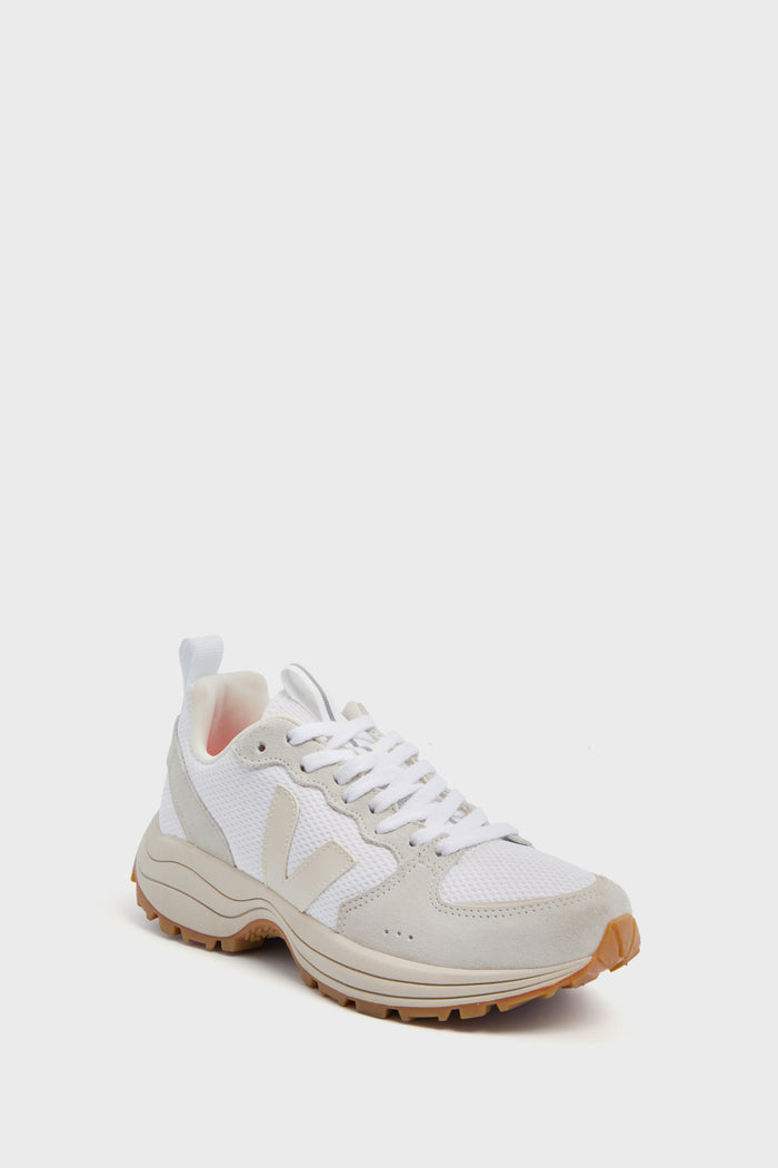 The VEJA sneaker features a white and beige mesh and suede upper, white laces, and a tan rubber sole, highlighting sustainable design crafted from recycled materials.