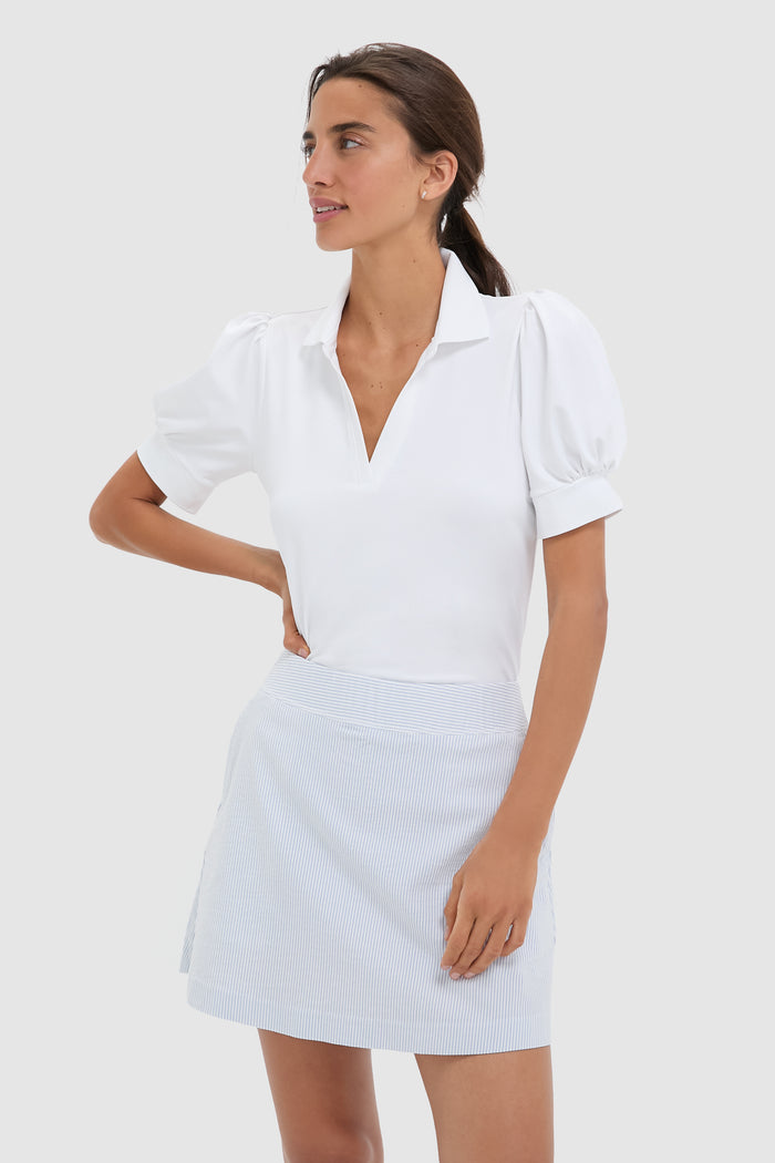A woman in a Tnuck Sport white puff sleeve polo and blue skirt, enjoying comfort and SPF protection.
