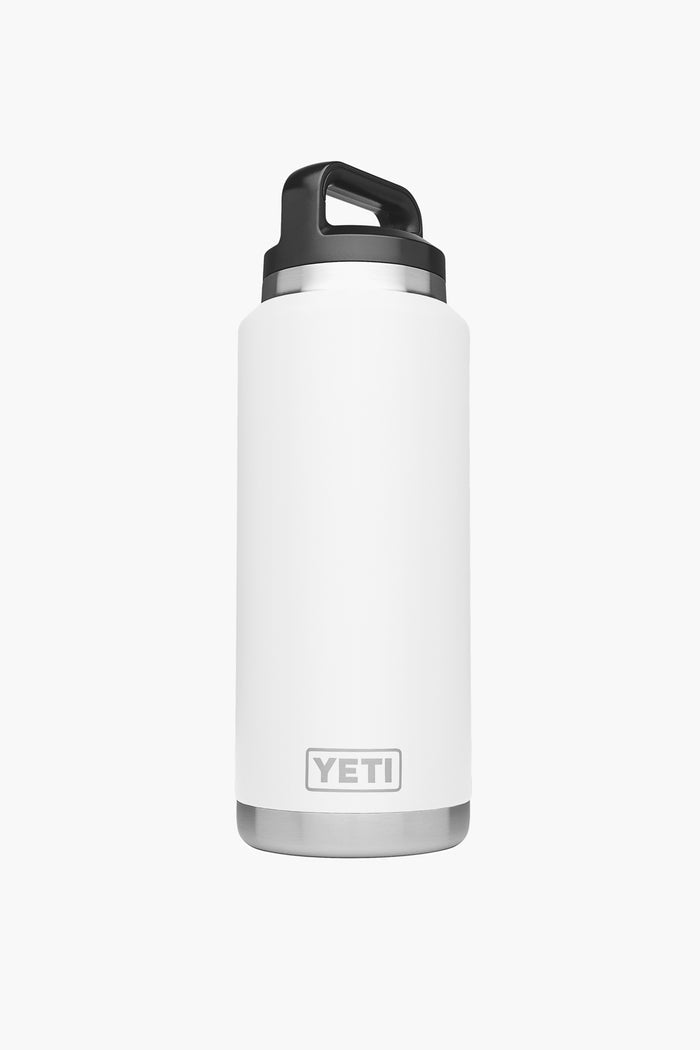 A white YETI Rambler Bottle with a black screw-on lid and handle stands upright. This stainless steel water bottle features vacuum insulation to keep beverages hot or cold for hours.