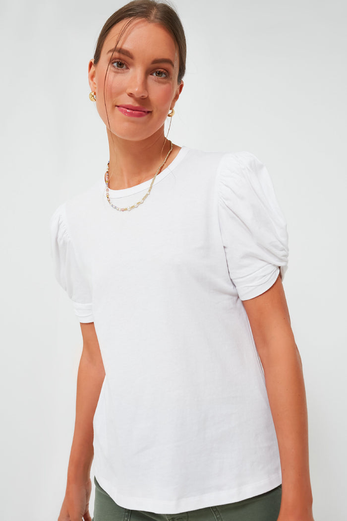 A woman in a Pomander Place White Vesty Puff Sleeve Crewneck, styled with gold earrings and a gold chain necklace, highlights the chic puffed shoulders and comfortable loose-fit cotton design.