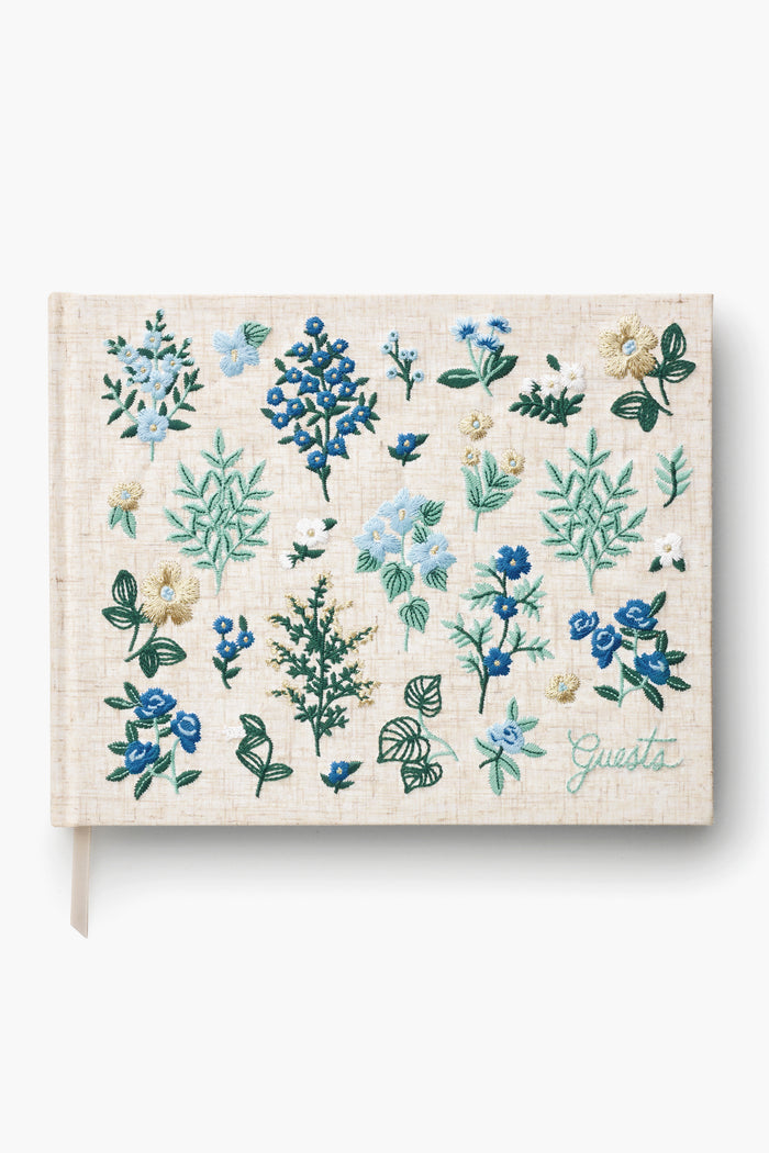 The Rifle Paper Co. beige hardcover guest book, titled "Guests," features green lettering and blue, green, and white floral embroidery—making it a charming keepsake for special occasions.