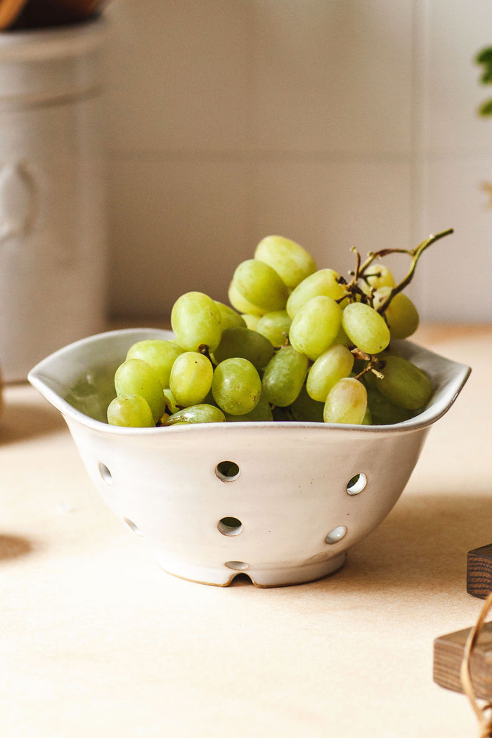 A cluster of green grapes sits in a Farmhouse Pottery, Inc white berry bowl on a light countertop.